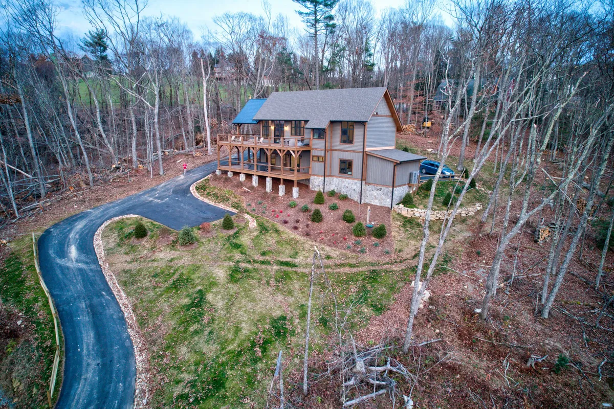 A peaceful exterior shot of the house and its driveway, framed by trees and natural surroundings. The scene conveys seclusion and serenity, with the home nestled in a wooded landscape ideal for peaceful workdays and relaxation.
