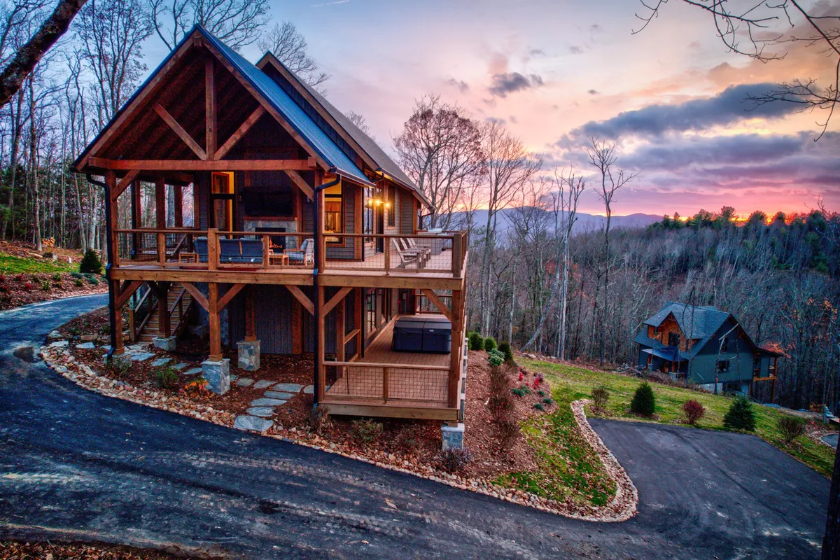 This exterior image captures The Dire Wolf's welcoming facade, the inviting porch, a bubbling hot tub, and a backdrop of sunset-lit trees. The tranquil ambiance highlights opportunities to relax on the porch, soak in the hot tub, and take in the Blue Ridge vistas.