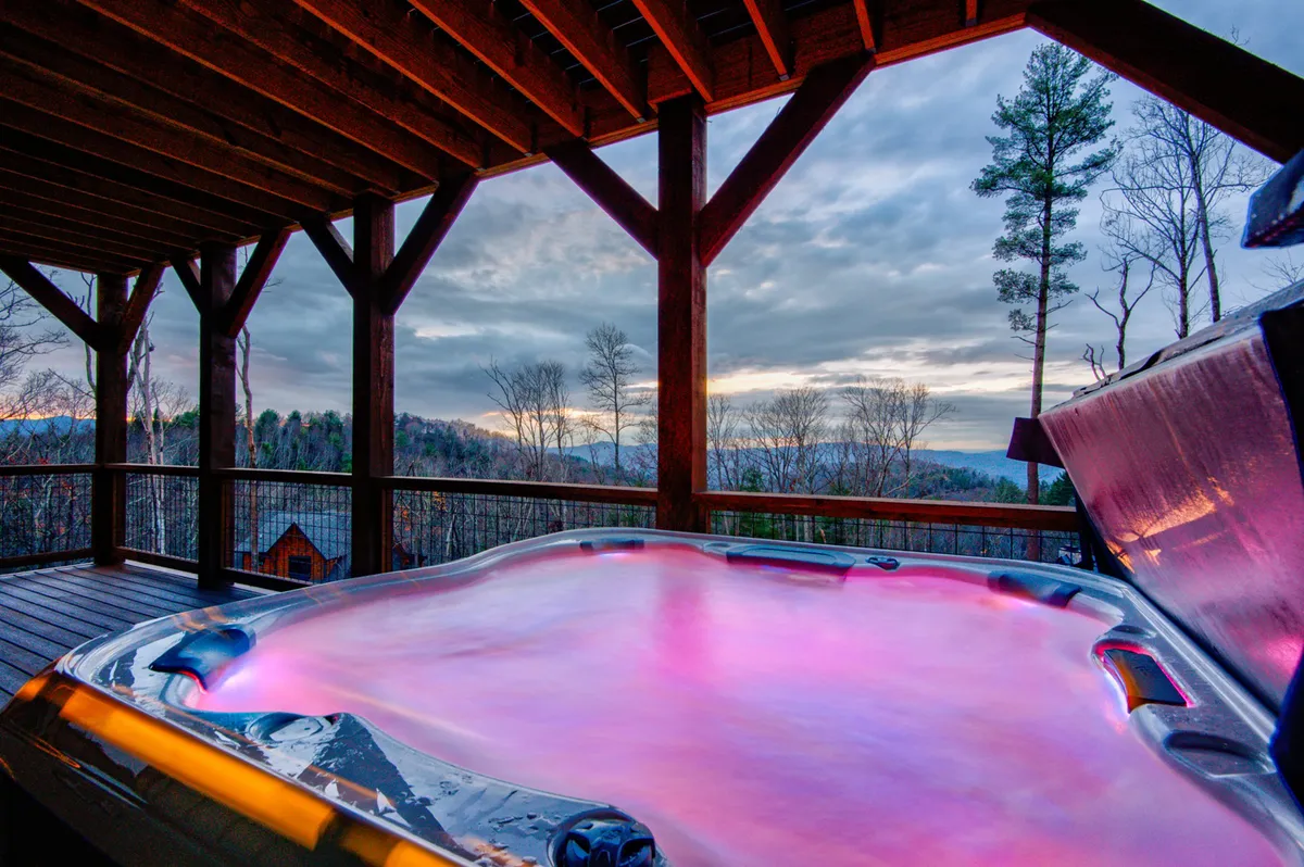This image features a hot tub nestled on a wooden deck, framed by sturdy wooden beams and offering a stunning scenic view of the mountains. The tranquil atmosphere is enhanced by the soft natural light and the sense of seclusion, perfect for relaxing and soaking in the beauty of the Blue Ridge Mountains.