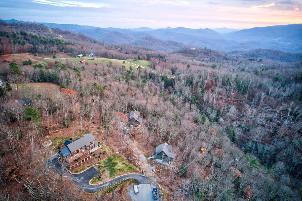 An exterior view of the main house nestled in a lush forest with a dramatic mountainous backdrop. It features expansive woodland surroundings, suggesting proximity to trails and opportunities for hiking, stargazing, and nature walks—all central to the text's sense of exploration.