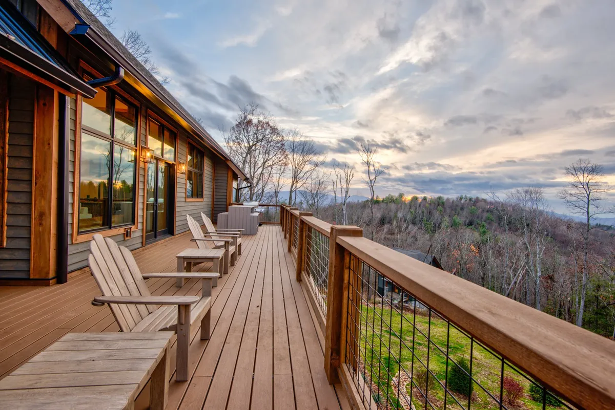 A panoramic exterior shot featuring a deck with comfortable wooden chairs overlooking rolling hills and a vibrant sunset sky. The image evokes peaceful moments of socializing, enjoying a glass of wine, and soaking in the stunning landscape.
