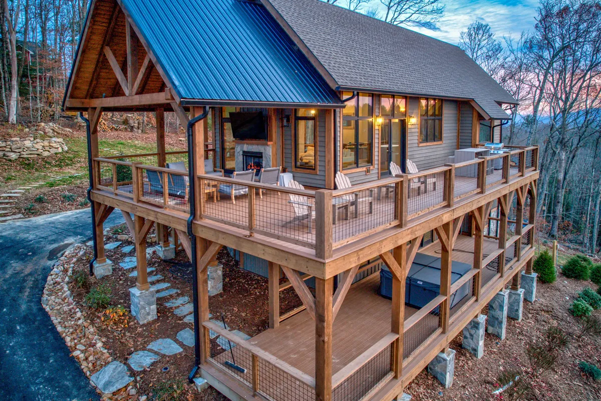 An inviting wooden deck with a spacious outdoor seating area, large windows reflecting the home's interior warmth, and surrounding trees. The setting is ideal for al fresco dining, morning coffee, or evening relaxation, connecting the interior spaces with nature.