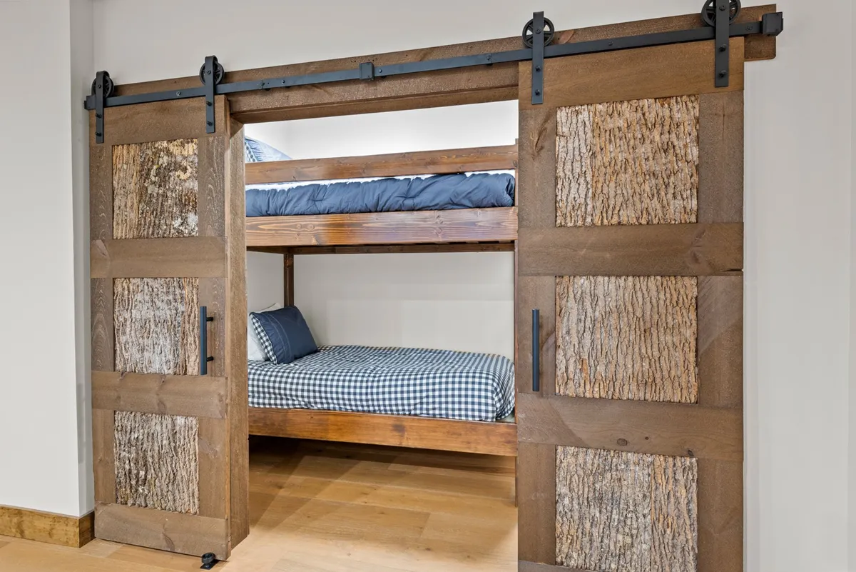A cozy bunk room with charming wooden bunk beds, sliding barn doors, and warm wood textures. The space feels inviting and is designed for both fun and restful nights, ideal for children or friends sharing the room.