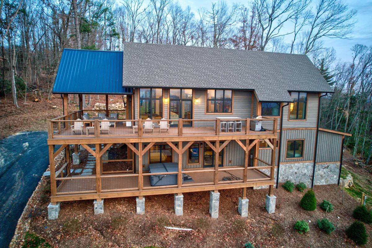 A view of the large deck attached to the wooden structure of the house, featuring a stone foundation and expansive windows. The deck appears inviting for relaxation or outdoor work, with ample space for seating and wide views of the surrounding natural landscape.