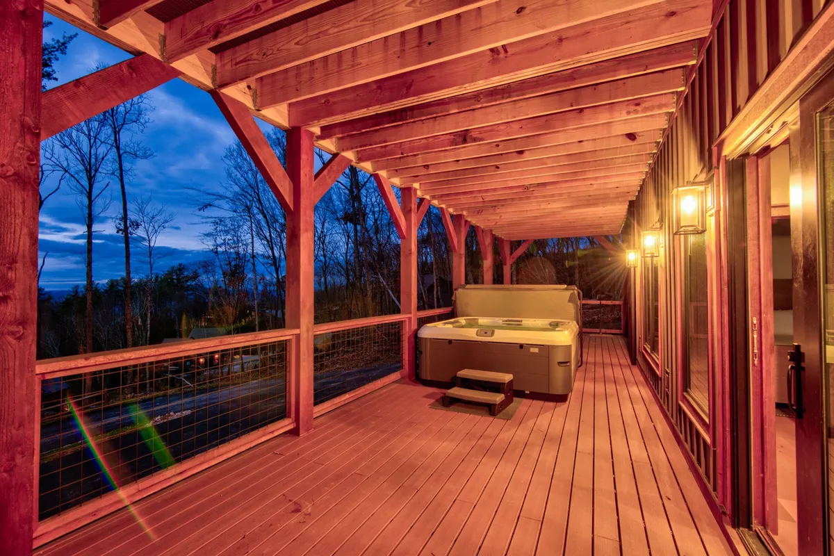 A close-up view of the hot tub on a wooden deck, accented by exposed beams and warm outdoor lighting. The image evokes serene evenings spent soaking in the tub while enjoying far-reaching sunset views and tranquil moments under the stars.
