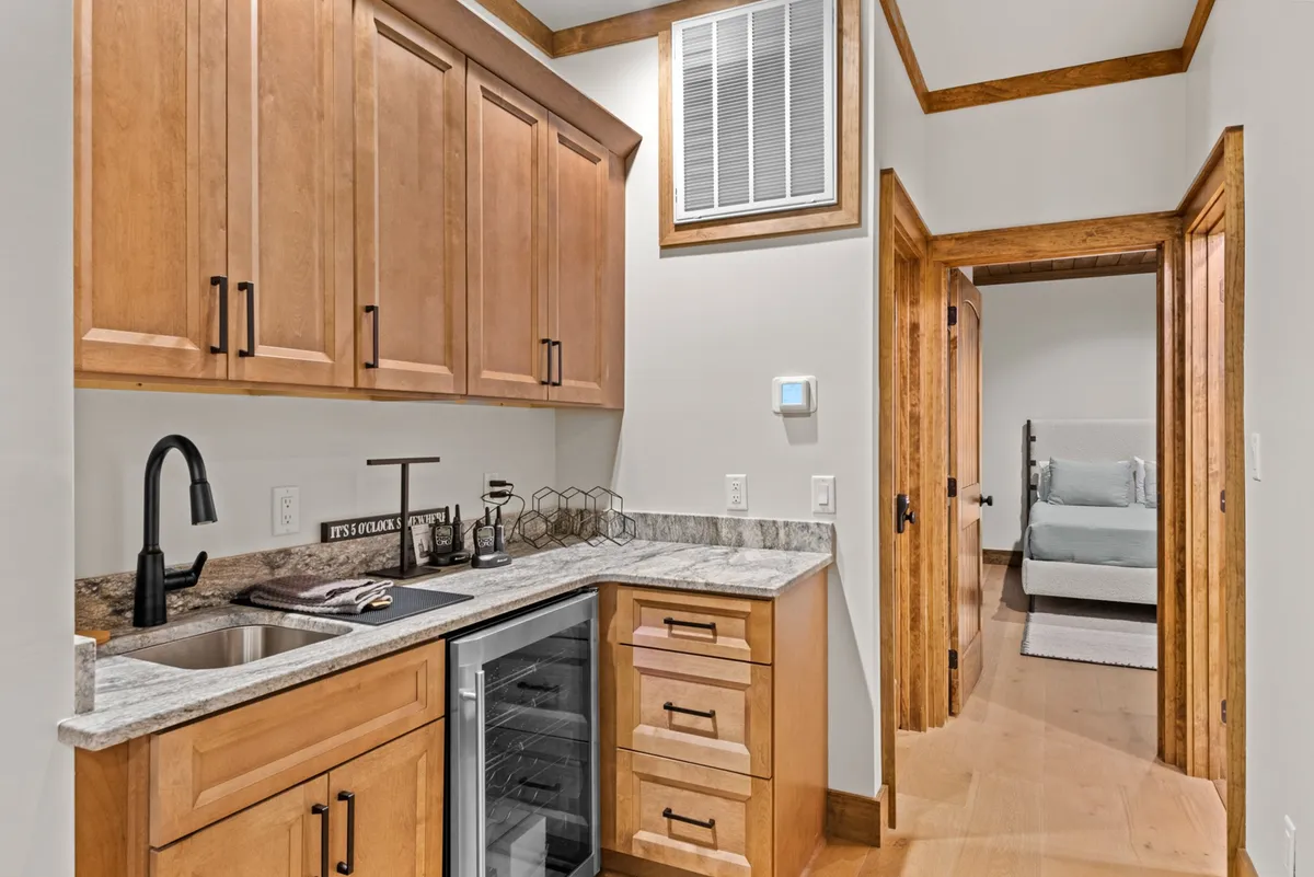This image displays a kitchenette with a granite countertop, wooden cabinetry, and a doorway leading to a bedroom—an ideal wet bar or snack zone setup for socializing and refreshing drinks during gatherings.