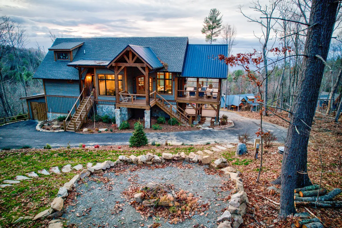 A welcoming exterior shot featuring a spacious wooden deck, cozy fire pit area, and the inviting structure of the house surrounded by serene nature. The fire pit is set up for gatherings, and the deck offers an expansive view of the sunset and nearby woods, emphasizing outdoor family experiences.